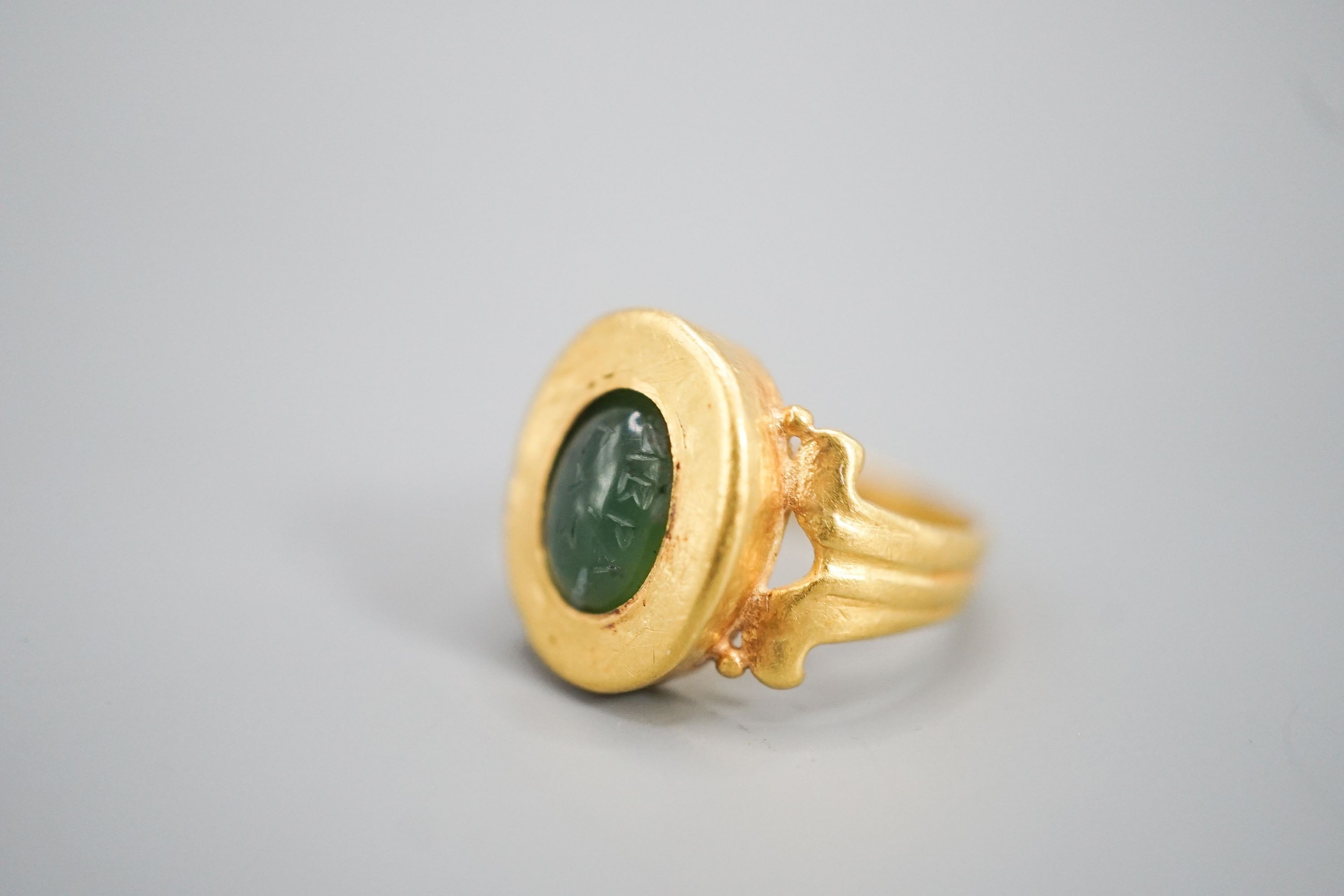 An antique yellow metal and carved nephrite? oval ring, size H, gross 4 grams (the stone is loose in situ and needs re-setting).